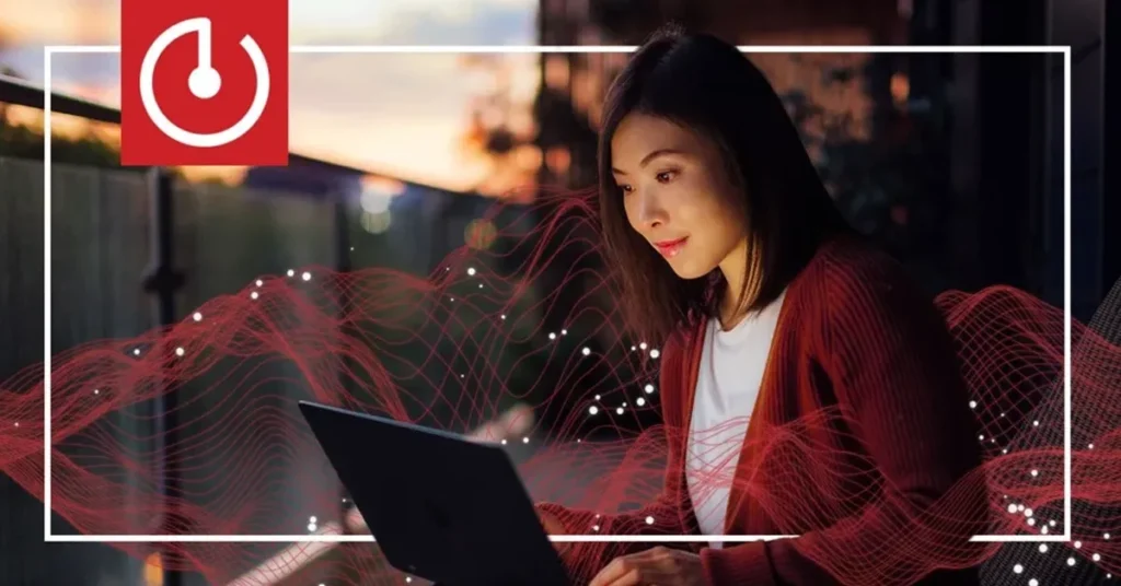 Mujer usando una laptop al atardecer, con ondas rojas de energía alrededor y un logotipo de encendido en la esquina superior izquierda.