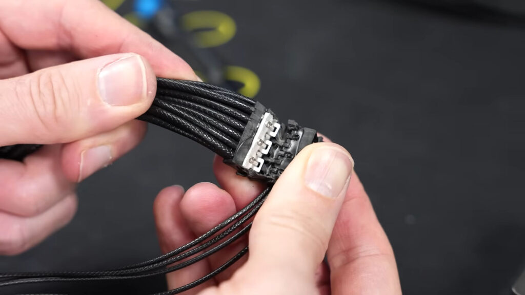 Conector del cable ASUS ROG Equalizer, con múltiples hilos negros trenzados, destacado sobre fondo oscuro, mostrando detalles del conector.