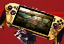 Controlador de videojuegos personalizado en tonos amarillos y negros, mostrando un juego de conducción en su pantalla, sostenido por un brazo robótico.