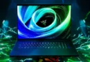 Laptop Razer Blade 18 con pantalla iluminada en azul y verde, fondo dinámico con efectos de luces y colores vibrantes.