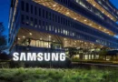 Edificio moderno de Samsung iluminado en la noche, con un gran logotipo blanco en la entrada y vegetación en primer plano.