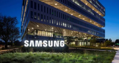Edificio moderno de Samsung iluminado en la noche, con un gran logotipo blanco en la entrada y vegetación en primer plano.