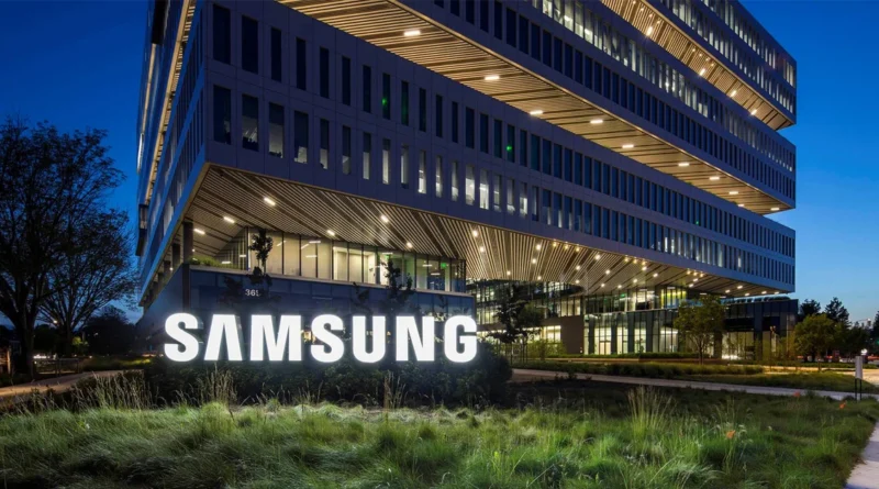 Edificio moderno de Samsung iluminado en la noche, con un gran logotipo blanco en la entrada y vegetación en primer plano.