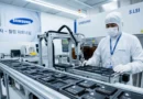Trabajador en un laboratorio de Samsung, usando equipo de protección, manipulando productos en una línea de ensamblaje. Fondo tecnológico.