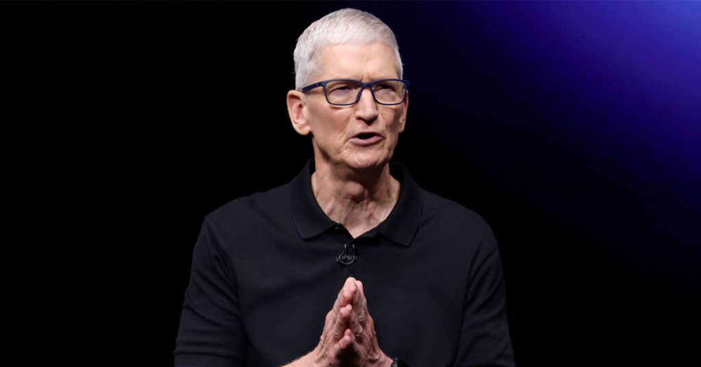 Tim Cook, director de Apple, con polo negro y gafas, gesticulando mientras habla frente a un fondo oscuro y luces moradas.