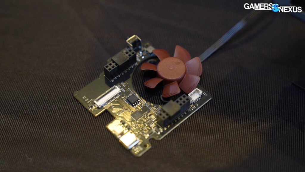 Placa de circuito impreso con un ventilador marrón, conectores y puertos USB, sobre un fondo negro texturizado.