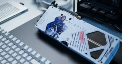Tarjeta gráfica Zotac RTX 5070 AMP PRAGMATA con diseño artístico de personajes, colores blanco y azul, sobre una superficie oscura con un teclado.