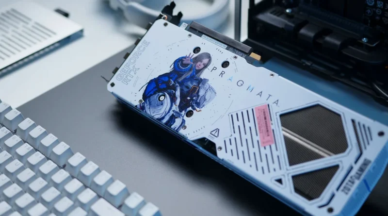 Tarjeta gráfica Zotac RTX 5070 AMP PRAGMATA con diseño artístico de personajes, colores blanco y azul, sobre una superficie oscura con un teclado.