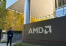 Edificio moderno de AMD con un cartel grande en primer plano, rodeado de vegetación y árboles con hojas amarillas en otoño.