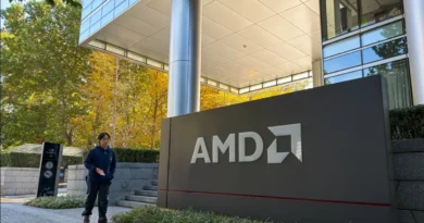 Edificio moderno de AMD con un cartel grande en primer plano, rodeado de vegetación y árboles con hojas amarillas en otoño.