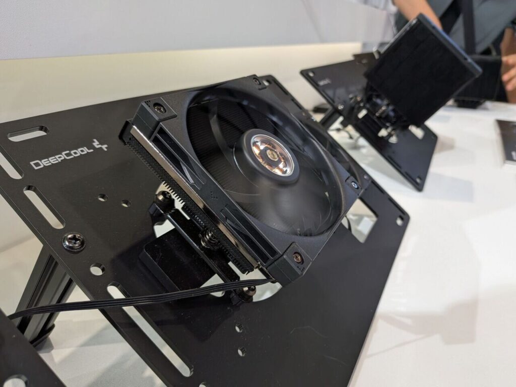 En el centro, un ventilador negro de DEEPCOOL montado sobre una base, con un diseño minimalista y moderno, exhibido en una presentación.