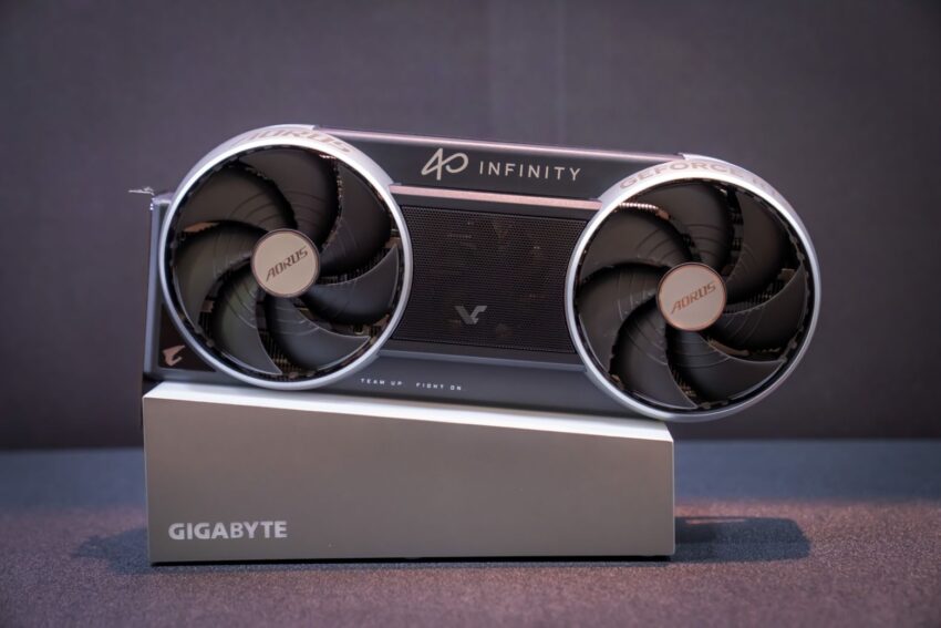 Tarjeta gráfica Gigabyte con diseño moderno, dos ventiladores grandes y colores negro y plateado, sobre una base con el logo de Gigabyte.
