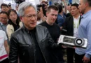 Jensen Huang sostiene una GPU GTX 1080 firmada, rodeado de personas en un evento, todos con sonrisas y cámaras.