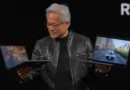 Hombre con cabello canoso sostiene dos laptops, una muestra un juego y la otra una escena de conducción, frente a fondo negro.