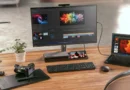Monitor y portátil en un escritorio, con equipo de edición y cámara; visual de productividad y tecnología.