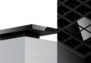 Dispositivo rectangular negro en la parte superior de un soporte blanco, junto a una estructura negra con diseño de rejilla.