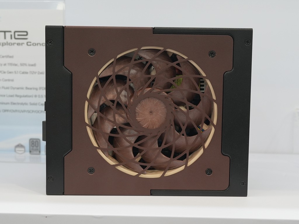 Fuente de alimentación modular con ventilador central, color marrón y negro. Diseño industrial con rejilla en espiral y acabados simplistas.