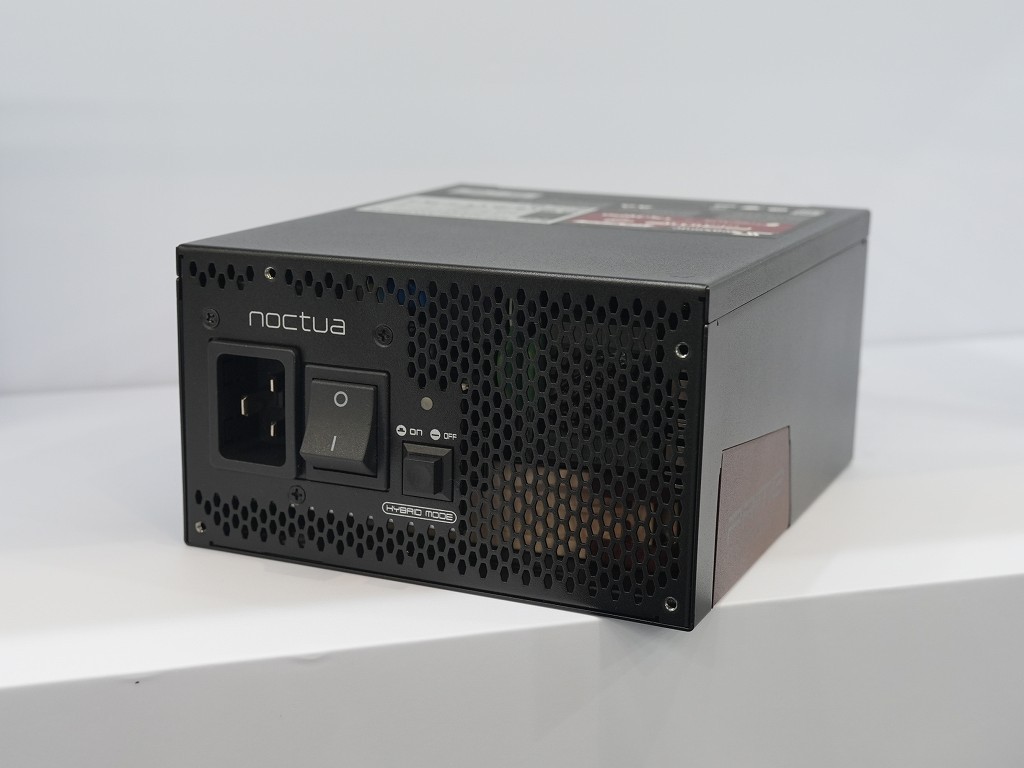 Fuente de alimentación Noctua con diseño compacto, color negro y rejilla metálica, mostrando el conector de corriente y el interruptor.