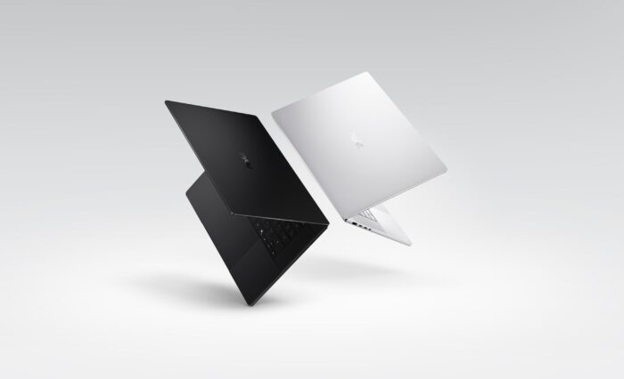 Dos laptops en ángulos opuestos, una en negro y otra en plata, flotan sobre un fondo gris claro, destacando sus diseños elegantes.