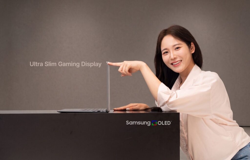 Mujer sonriente señala un monitor Ultra Slim Gaming Display en un fondo neutro, con el logo de Samsung OLED visible en la base.
