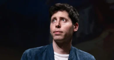 Hombre con chaqueta azul y camiseta blanca, mirando hacia arriba con expresión pensativa, fondo desenfocado oscuro.