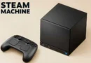 Steam Machine negra en un fondo beige, acompañada de un control; destaca su diseño compacto para juegos.
