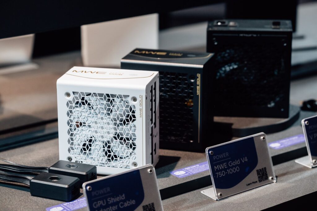 Fuentes de alimentación MWE Gold V4 en tonos blanco y negro, con paneles laterales texturizados y accesorios en una exhibición.