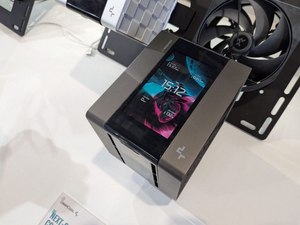 Dispositivo compacto con pantalla táctil, mostrando hora y gráficos de energía. Colores oscuros y diseño moderno, con ventilador al fondo.