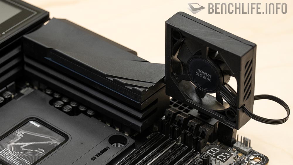 Placa base negra con disipador y fan AORUS en la esquina, destacando conectores y detalles de diseño en un fondo claro.