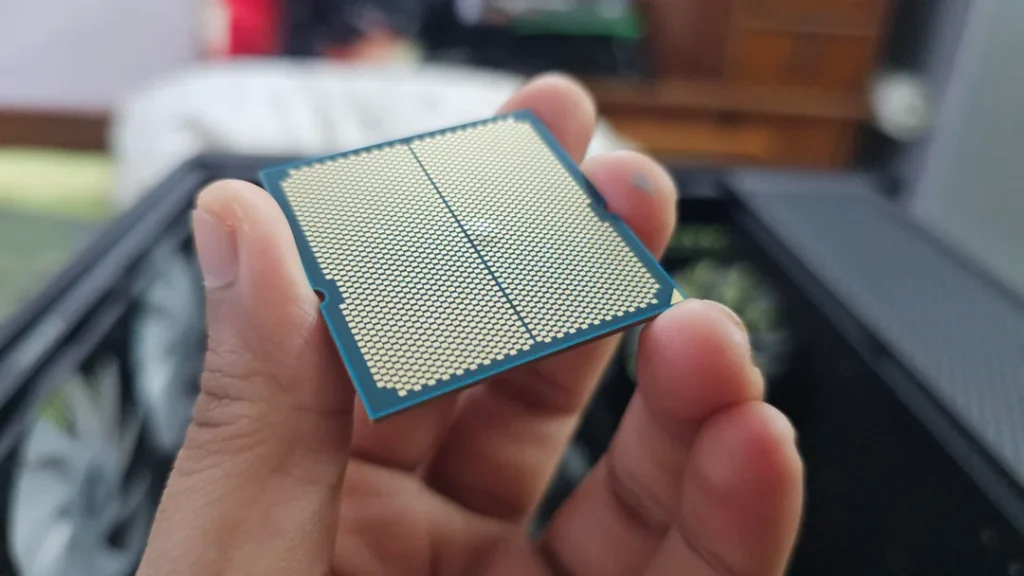AMD Ryzen 9 9900X sostenido en mano, mostrando el diseño del procesador con pines, en un entorno de hardware.
