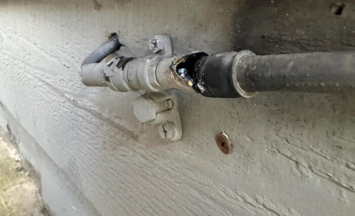 Conexión de cable de red dañada, mostrando quemaduras y un desglose en el revestimiento, sobre una superficie de pared gris.